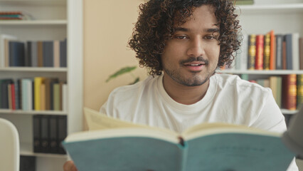 Man reads book and turns a page at a table in a library building with bookshelves behind him  concentration study. © Krakenimages.com