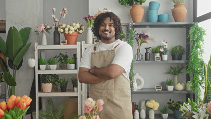 Naklejka premium Man florist in apron with arms crossed amid potted flowers, shelves of plants, pots and vases in building; contentment.