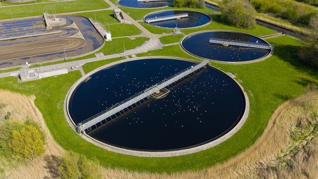 Aerial view of RWZI Geestmerambacht wastewater treatment plant with circular tanks and seagulls on the water surface surrounded by green fields Netherlands.