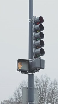 A traffic signal is displaying a hand symbol indicating not to cross while snow covers the ground in a city setting. Trees are visible in the background.