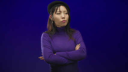 Obraz premium Woman in purple turtleneck wearing beret with crossed arms and one thumb up gesture in studio; wry amusement.