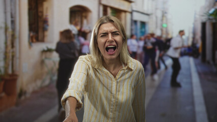 Fototapeta premium Woman screaming with arm outstretched and open hand, striped shirt, mouth open, eyes closed amid crowded street with blurred pedestrians; distress.