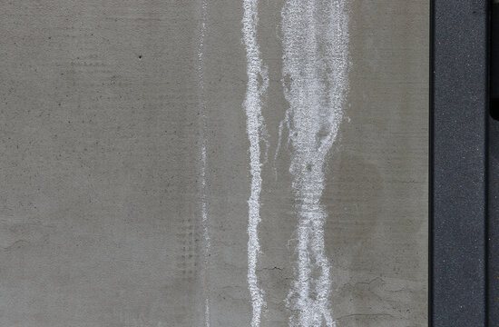 Close-up of white efflorescence salt deposits on a grey concrete wall.