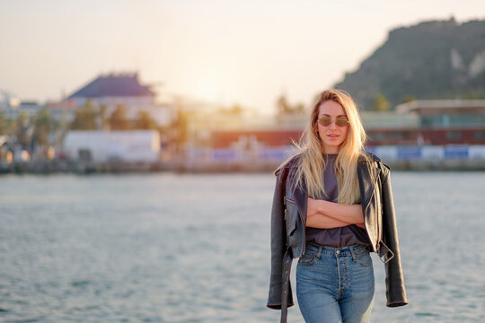 Young Fit Blonde Woman in Leather Jacket and Sunglasses at Sunset Harbor
