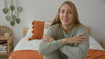Obraz premium Woman on bed sitting with arms crossed over knees and head tilted, smiling toward camera in studio; serenity.
