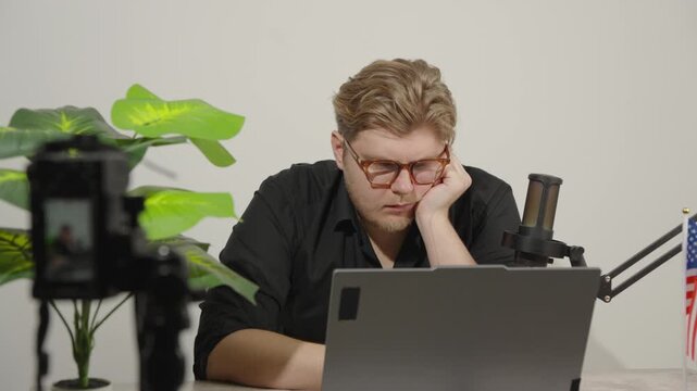 Bored male streamer sitting in front of laptop and camera