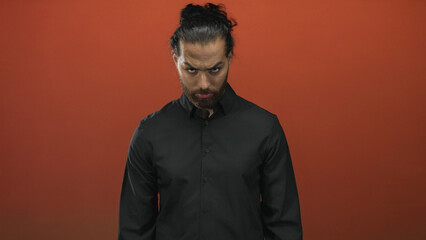 Fototapeta premium Man with beard wearing a black shirt and closed eyes looking down in an orange studio midshot; introspective calm.