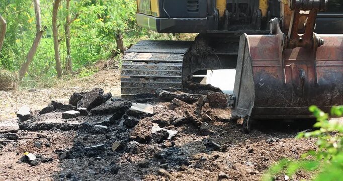 Excavator Digging Up Road Surface, Road construction and demolition, Excavator bucket digging, lifting broken asphalt and concrete debris, Excavator loading broken concrete at construction site