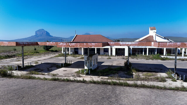 Aerial view of an abandoned roadside building with a weathered canopy and red tiled roof against the backdrop of Platberg mountain in iNtabazwe, Free State, South Africa.