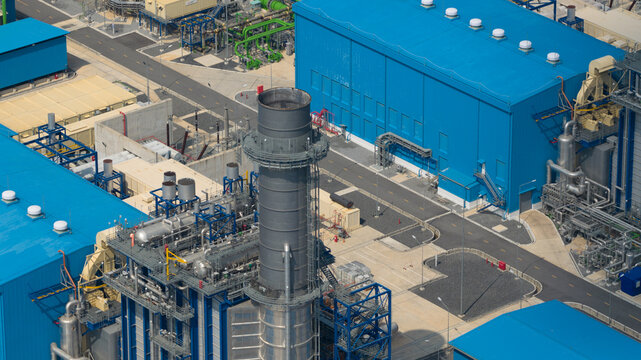 Aerial view of the Gulf PD Power Plant featuring large blue industrial buildings, a tall exhaust stack, and intricate piping systems under bright daylight in Map Yang Phon, Rayong, Thailand.