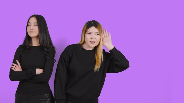 Two asian women eavesdropping and listening on purple background