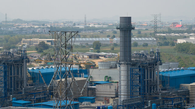 Aerial view of the GPD industrial power plant featuring blue factory buildings, tall exhaust stacks, and high-voltage electricity pylons under a hazy sky in Map Yang Phon, Rayong, Thailand.