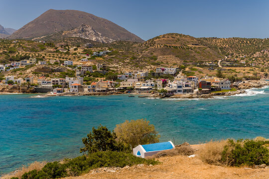 Looking over turquoise sea toward small coastal village and rugged mountains