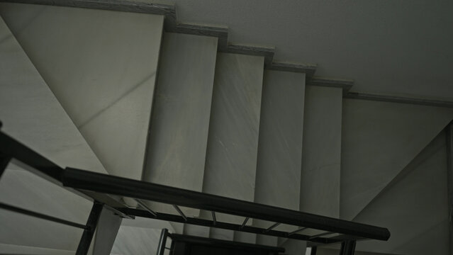 Marble staircase seen from above with black metal handrail and descending steps in building; minimalist solitude.