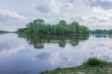Fototapeta premium a lush green island reflecting on the calm surface of a wide river.