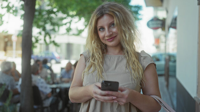 Woman holding smartphone and smiling on street while checking messages; contentment connection ease.