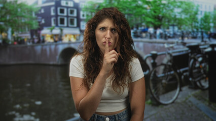 Fototapeta premium Woman with finger to lips for silence on amsterdam street by canal and parked bicycle; quiet secrecy.