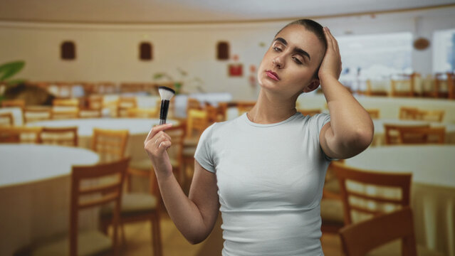 Woman holding makeup brush with hand on forehead in a dining building, round tables and chairs visible; fatigue.