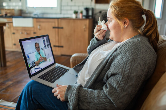 Sick woman using nasal spray during telehealth consultation at home