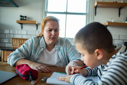 Concerned parent helping child with homework at kitchen table at home
