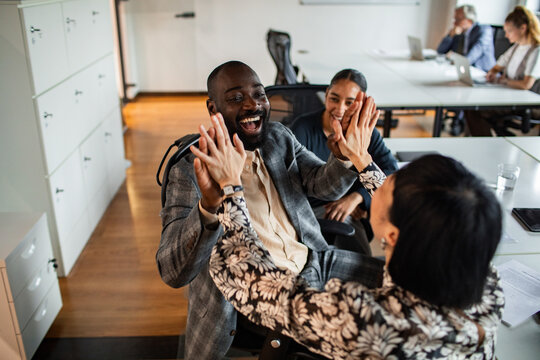 Diverse coworkers celebrating success with high five in modern office