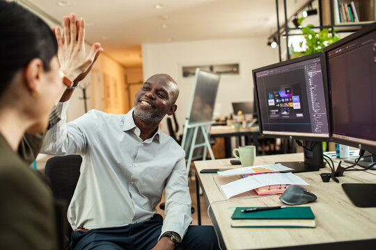 Coworkers high-fiving after design success in modern office