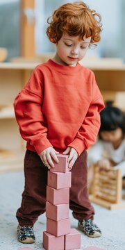 Red haired child stacking toy blocks in preschool playroom