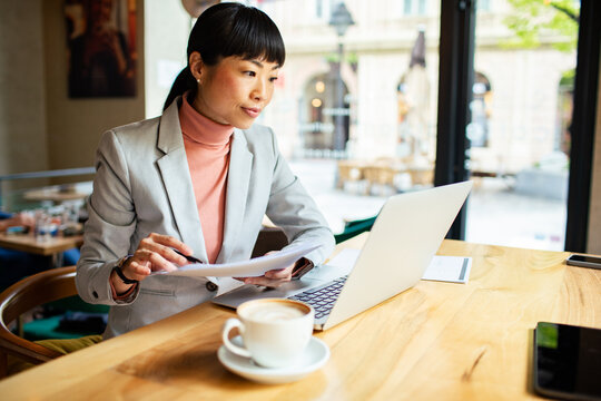 Businesswoman working on laptop with papers in coffee shop