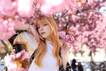 Fototapeta premium Beautiful young girl posing near blossoming sakura tree outdoors. Space for text