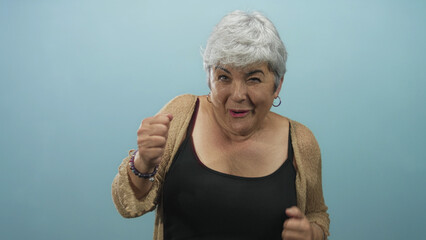 Woman raising arms and smiling with exposed shoulders and hoop earrings against a blue studio backdrop, wearing a cardigan and tanktop  joy celebration. © Krakenimages.com