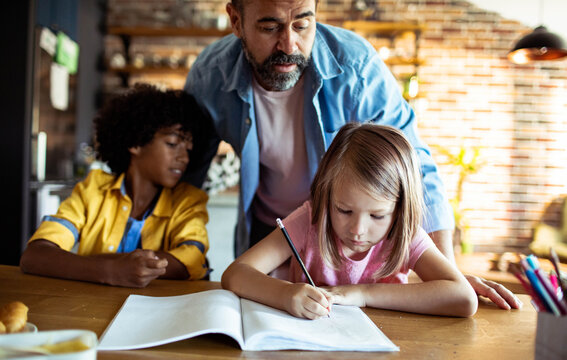 Father helping children with homework at kitchen table