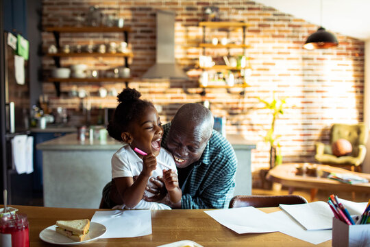 Grandfather hugging granddaughter while drawing at kitchen table
