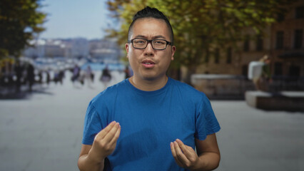 Man clenches fist on street in urban plaza wearing blue tshirt and glasses while standing before blurred pedestrians and benches  determination. © Krakenimages.com
