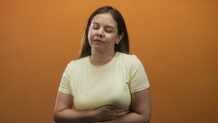 Obraz premium Young caucasian woman holding her stomach and touching her throat in an orange studio; discomfort nausea.