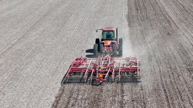 Aerial rear view of a red tractor  Pulling a  Double Fold Cultivator for spring field preparation.