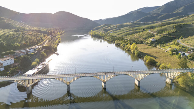 Aerial view of Barca de Alva bridge over the Douro River surrounded by lush green hills and vineyards in Figueira de Castelo Rodrigo, Distrito da Guarda, Portugal.