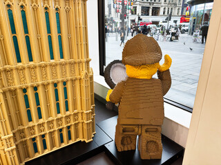 Naklejka premium Lego detective sculpture with magnifying glass beside Big Ben model in a London UK shop window display, playful brick art representing landmark, tourism and urban street scene