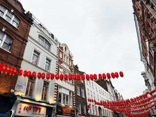 Naklejka premium Red lanterns and Chinatown street decorations over a London, UK shopping street with historic brick buildings and restaurants celebrating cultural festival