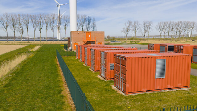 Aerial view of rows of orange industrial containers and a brick utility building near wind turbines on a sunny day in Middelharnis, Zuid-Holland, Netherlands.