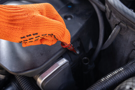 A person uses a dipstick to check the oil level in a car engine while working in a garage during the day