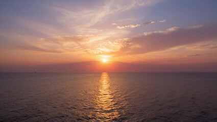 Obraz premium Sun dips low, painting sky in warm hues. Golden light reflects across calm ocean surface. Soft clouds drift as day fades into evening. Peaceful, serene, and tranquil atmosphere dominates scene