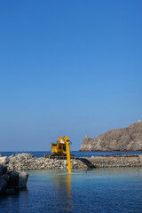 Fototapeta premium Coastal construction excavator working on rocky breakwater featuring marine construction, waterfront engineering and industrial coastal development