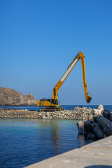 Fototapeta premium Marine infrastructure construction featuring excavator on stone breakwater, coastal engineering and waterfront industrial development