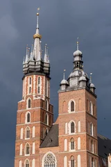 The asymmetric towers of St. Mary's Basilica in Krakow. A detailed view of the Gothic brick church's spires against a dark, stormy sky in the Main Market Square, Poland. © Pat dream