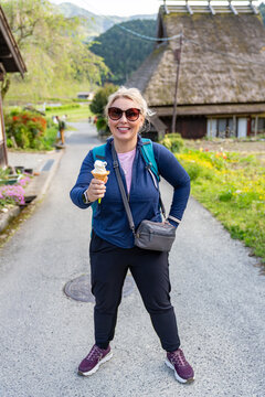 Blonde tourist woman holds an ice cream cone while exploring a traditional Japanese village Miyama