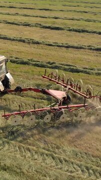 Close up drone shot of agricultural machinery tedding dry grass in summer. Red rotary rake attachment processing hay on a green meadow for livestock feed production