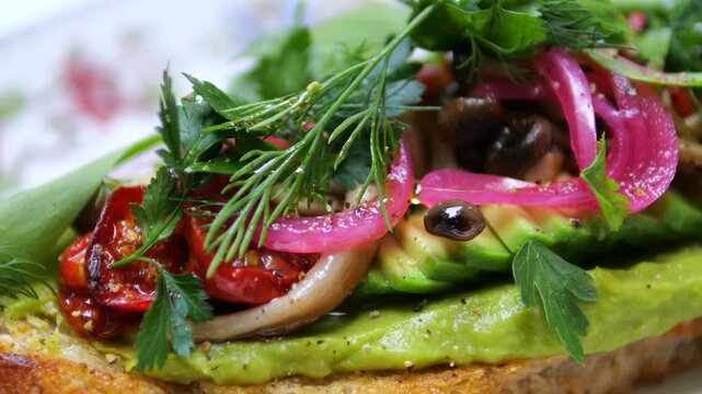Freshly made bruschetta with avocado spread, topped with grilled tomatoes, pickled red onions, mushrooms, and fresh dill and parsley, presented on a plate as a healthy gourmet appetizer