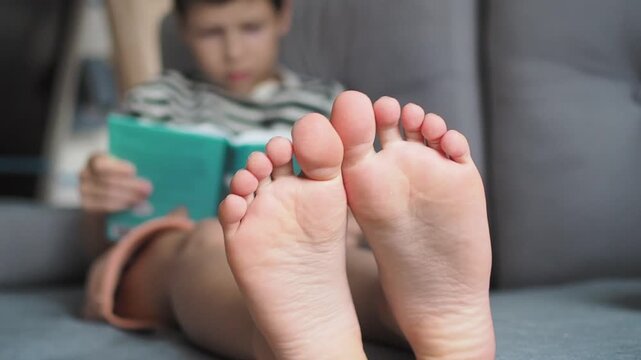 Boy's bare feet close up to camera. Boy is reading in the living room on the couch