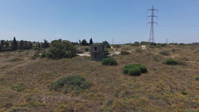 Aerial view of abandoned rural buildings surrounded by dry scrubland vegetation with a large electricity pylon in israel

