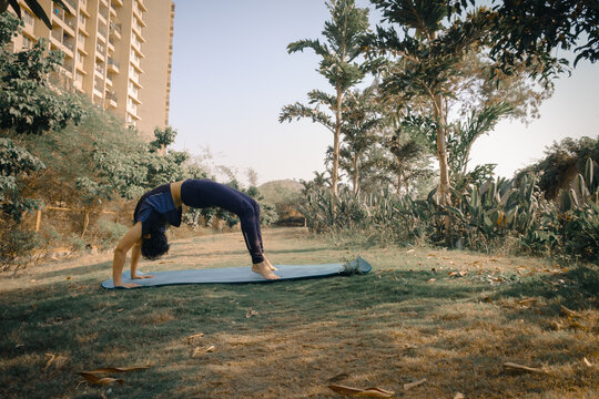 Woman doing Urdhva Dhanurasana yoga (Wheel Pose or Upward Bow Pose) in the garden. International Yoga Day